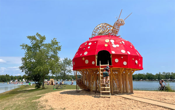 A wooden, mushroom-shaped structure near a lake.