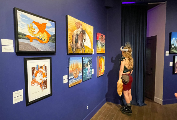 A woman stand in front of a group of artworks hanging on a blue wall.