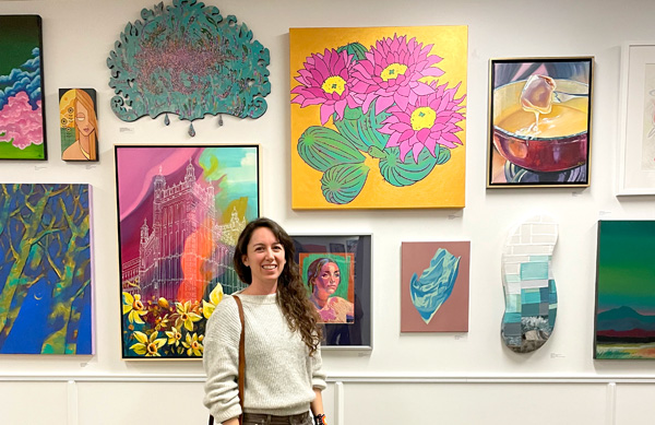 Cara standing in front of many paintings group together on a gallery wall.