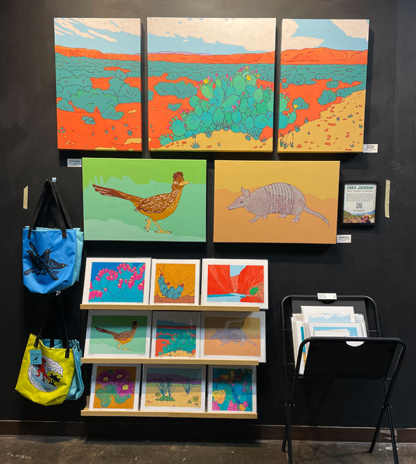 Original paintings of canyons, armadillo, and roadrunner, hanging over art prints.